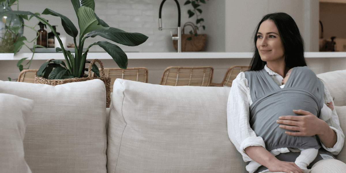 Newborn Baby Carrier in Grey Color worn by Woman sitting in a Couch